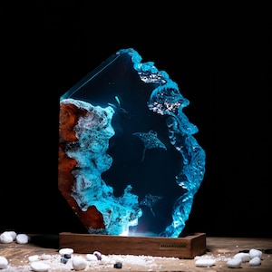 May include: A blue resin sculpture of a manta ray swimming in the ocean. The sculpture is set on a wooden base with the text "BREAKWOODEN" on the front.