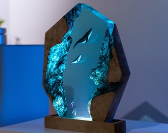May include: A blue resin sculpture of a whale swimming in a blue and green ocean. The sculpture is set in a wooden base.