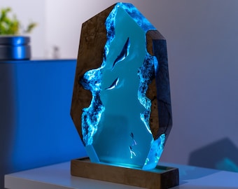 May include: A decorative wooden sculpture with a blue resin center, featuring a design of swimming fish. The wood has a natural, dark brown grain, and the resin glows with a soft blue light. The sculpture is mounted on a wooden base.