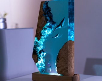 May include: A blue resin sculpture with a wooden base, depicting a scene of fish swimming in a blue ocean. The resin is clear and allows the viewer to see the fish swimming inside. The wooden base is dark brown and has a natural wood grain.