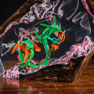 May include: A clear resin diorama featuring a green serpentine creature and an orange humanoid figure with blue accents. The scene is set against a dark, swirling background with pink and black textured rock formations and wisps of white smoke.