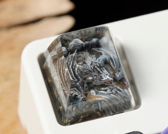 May include: A custom keyboard keycap featuring a detailed dragon sculpture. The keycap is clear with a gray and black dragon design, and a red accent on the dragon's mouth. The keycap is set on a white keyboard.
