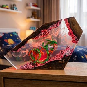 May include: A decorative resin lamp featuring a green serpentine dragon figure encased within a clear, angular block. The piece incorporates dark wood accents and textured, pink-hued rocky elements, with internal lighting creating a glowing effect.