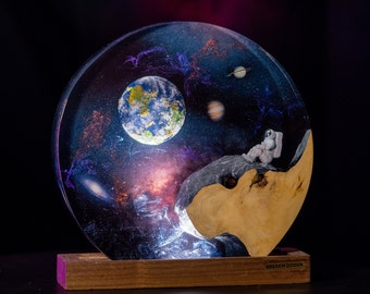 Può includere: Scultura rotonda in resina raffigurante una scena galattica con una figura di astronauta. La scultura presenta una base in legno e una rappresentazione dettagliata della Terra, Giove e Saturno. La parola "BREAKWOODEN" è visibile.