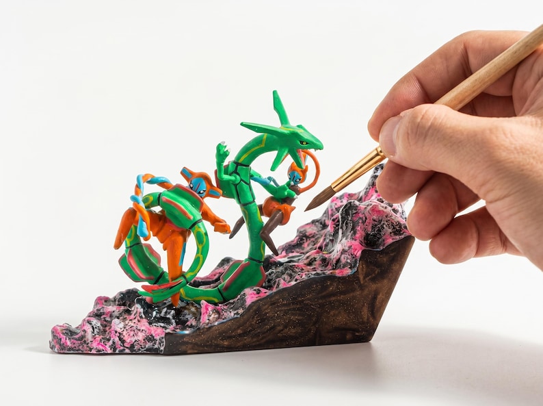 May include: A green serpentine dragon figure and an orange humanoid figure with blue accents positioned on a textured, rocky base with black and pink details. The figures are sculpted in a dynamic pose, with the dragon coiled around the base.