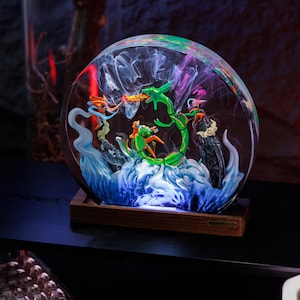 May include: A circular resin lamp featuring a green serpentine creature and orange figures amidst swirling white and blue smoke effects. The piece is mounted on a rectangular wooden base with a small metal plaque labeled BREAKWOODEN.
