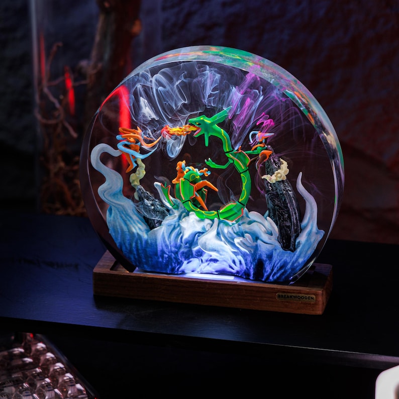 May include: A circular resin lamp featuring a green serpentine creature and orange figures amidst swirling white and blue smoke effects. The piece is mounted on a rectangular wooden base with a small metal plaque labeled BREAKWOODEN.