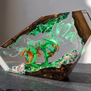 May include: A trapezoidal resin display piece featuring a green serpentine creature and an orange humanoid figure embedded within clear material. The base and top edges are made of dark wood, with swirling green smoke effects inside the resin.