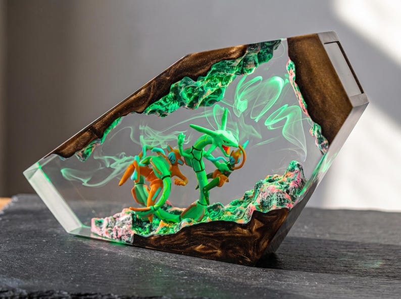 May include: A trapezoidal resin display piece featuring a green serpentine creature and an orange humanoid figure embedded within clear material. The base and top edges are made of dark wood, with swirling green smoke effects inside the resin.
