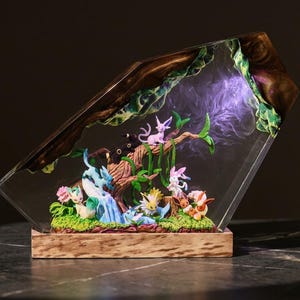 Può includere: Scultura decorativa in resina raffigurante una scena boschiva con personaggi dei cartoni animati colorati. L'opera d'arte è racchiusa in un blocco trasparente angolato con una base in legno. Il bordo superiore presenta un design in legno scuro e foglie verdi.
