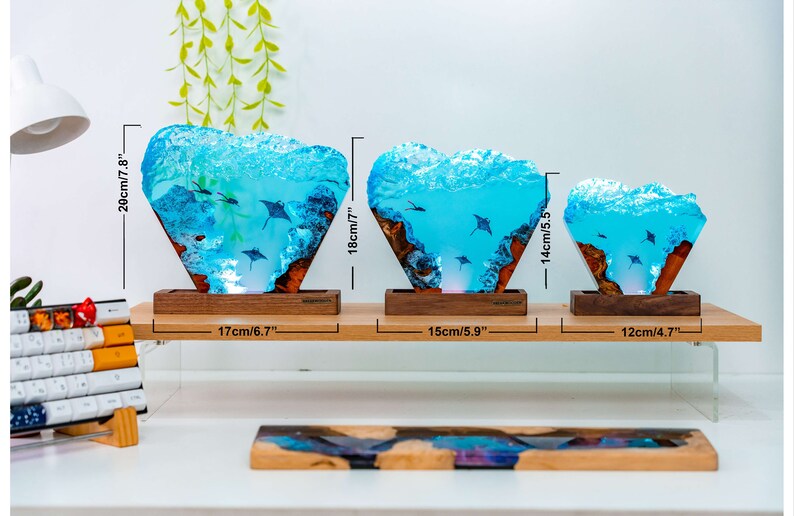 May include: Three resin lamps with a blue and white ocean scene and stingrays. The lamps are on a wooden base and are lit from the bottom. The lamps are 7.8 inches, 7 inches, and 5.5 inches tall.