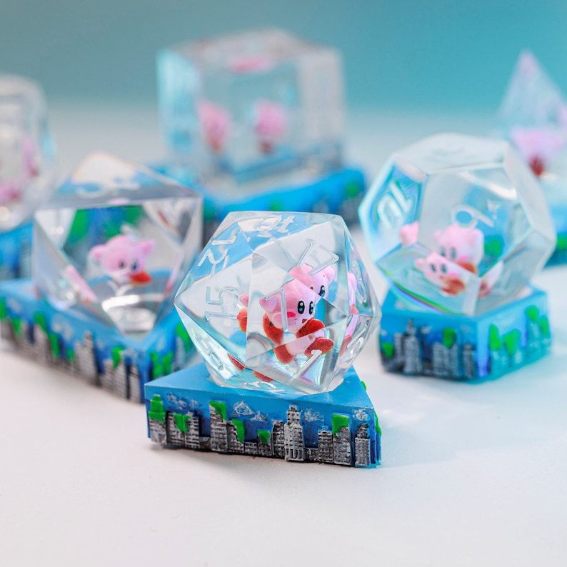 May include: Several clear, faceted dice featuring a pink character. Each die rests on a blue base with a cityscape design. The dice are in various geometric shapes, including a cube, a diamond, and a dodecahedron.