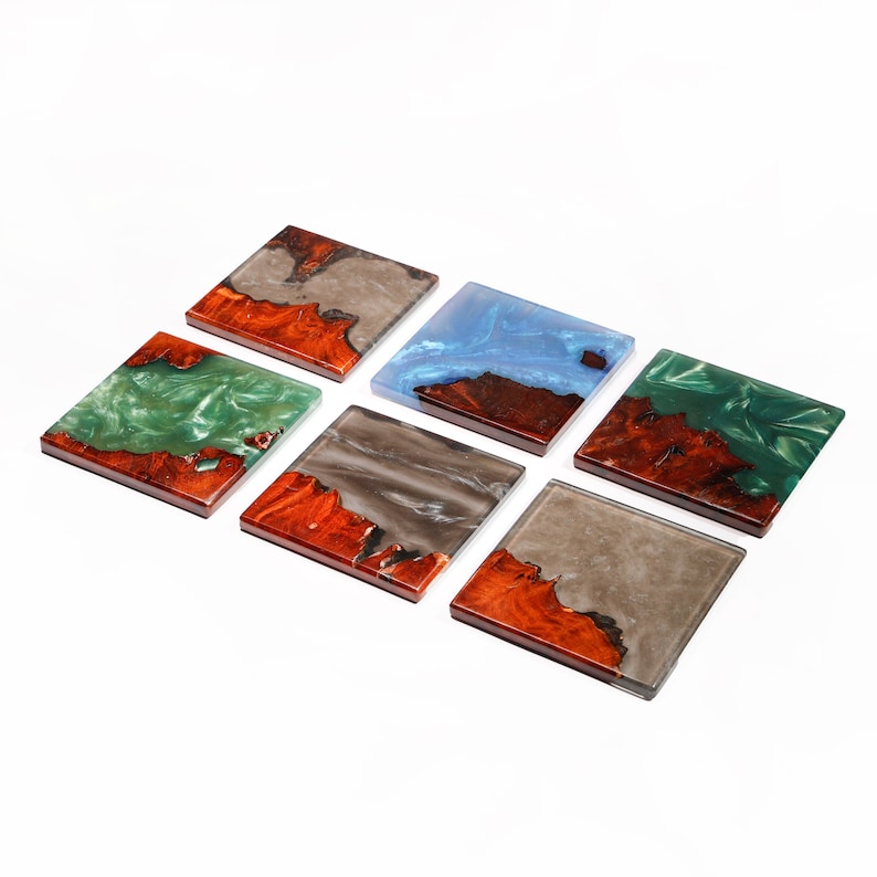 May include: Six square coasters with a wood and resin design. The coasters feature a variety of colors, including green, blue, gray, and brown. The wood has a reddish-brown hue, and the resin has a glossy finish. Each coaster is approximately 4 inches square.
