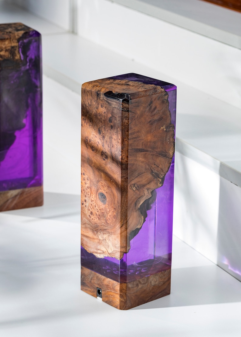 May include: A pair of rectangular wooden lamps with a striking design. The lamps feature a combination of natural wood grain and translucent purple resin. The wood has a rich, warm brown color, while the resin glows with a vibrant purple hue.