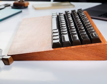 May include: A wooden keyboard with black keys and white keycaps. The keyboard is on a wooden base and has a brown finish.