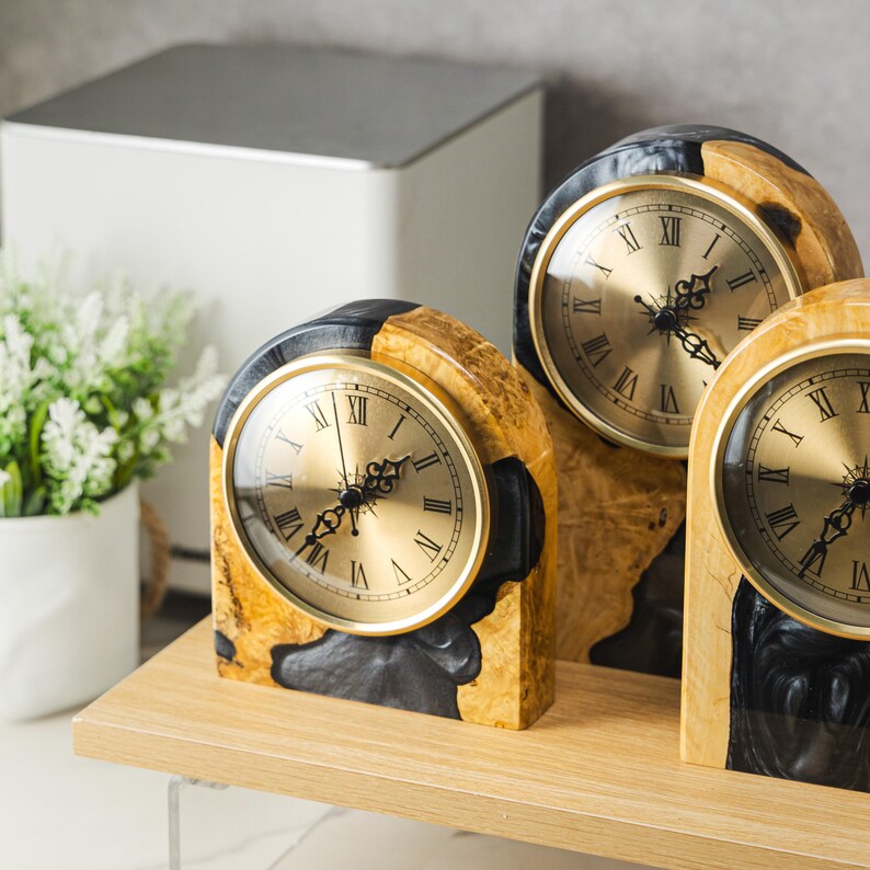 May include: Three decorative wooden clocks with gold-colored clock faces and Roman numerals. The clocks have a unique design, with a combination of light and dark wood tones. The clock faces are surrounded by a gold-colored frame.