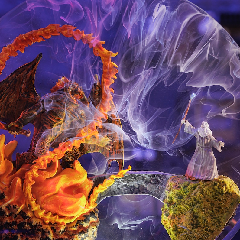 May include: A fantasy scene featuring a dragon engulfed in flames facing a wizard on a rocky outcrop. The dragon is brown and orange, with a fiery halo. The wizard is in a white robe, holding a staff. A stone bridge connects the two figures, with purple and white smoke.