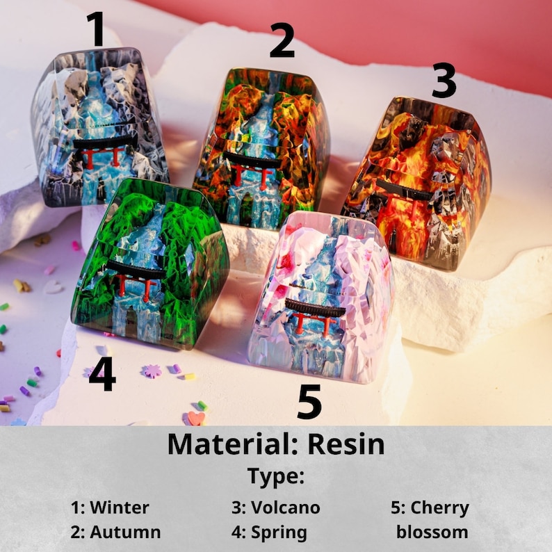 Puede incluir: Cinco teclas de resina con dise&ntilde;os de paisajes. Las teclas est&aacute;n etiquetadas como Invierno, Oto&ntilde;o, Volc&aacute;n, Primavera y Flor de cerezo. Cada tecla presenta una combinaci&oacute;n de colores diferente, incluyendo azul, naranja, verde y rosa. El material es resina.