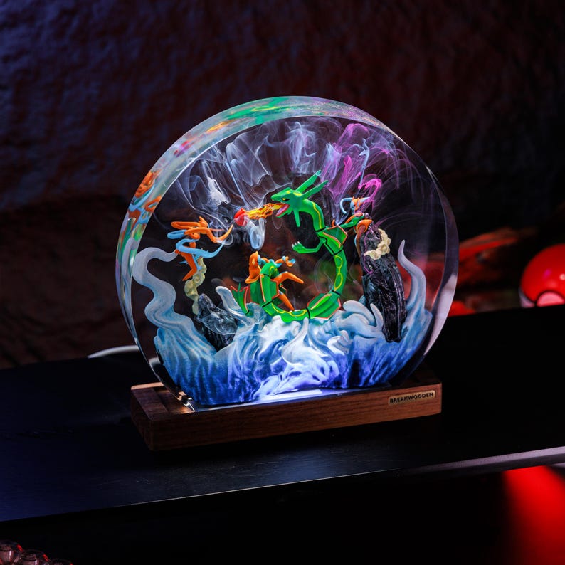May include: A circular resin lamp featuring a green serpentine creature and orange figures amidst swirling white and blue smoke effects, set on a rectangular wooden base with the text BREAKWOODEN engraved on a small metal plate on the front.