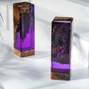 May include: Two rectangular decorative blocks. The base is a natural wood grain, transitioning to a vibrant purple resin. The resin is swirled with dark, smoky patterns. The blocks are displayed on a white surface.