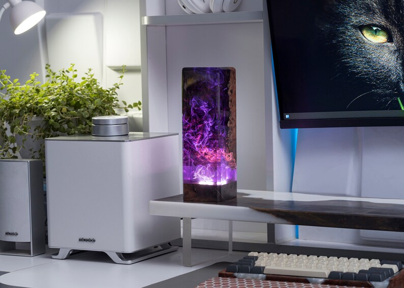 May include: A rectangular wooden and resin lamp with a vibrant purple and pink swirling design. The lamp is on a white desk with a computer monitor and keyboard in the background. The lamp is approximately 10 inches tall.