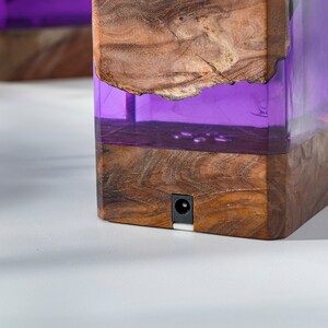 May include: Two wooden blocks with a rectangular shape, featuring a combination of natural wood and translucent purple resin. The wood has a visible grain and a rough edge. Each block has a small, round power port.