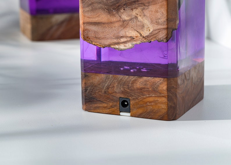 May include: Two wooden blocks with a rectangular shape, featuring a combination of natural wood and translucent purple resin. The wood has a visible grain and a rough edge. Each block has a small, round power port.