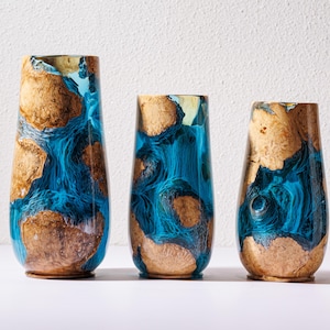 May include: Three decorative vases with a unique design. The vases feature a combination of wood and blue resin, creating a striking contrast. The wood has a natural, light brown color, while the resin has a vibrant blue hue. The vases are of varying sizes.