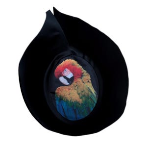 May include: A black hat with a round, colorful parrot design on the front. The parrot is facing left and has red, yellow, green, and blue feathers.