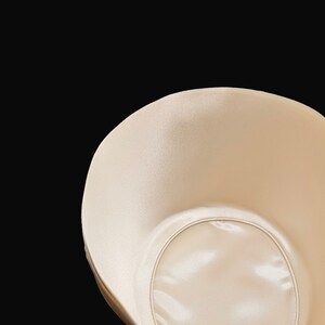 May include: A beige bra cup with a smooth, satin-like finish. The cup has a circular opening in the center.