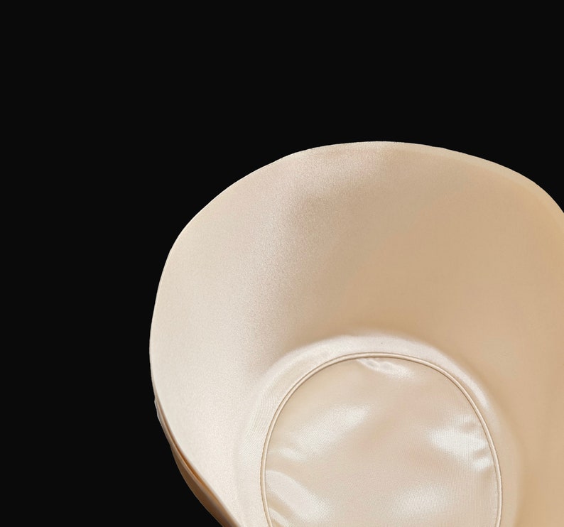 May include: A beige bra cup with a smooth, satin-like finish. The cup has a circular opening in the center.
