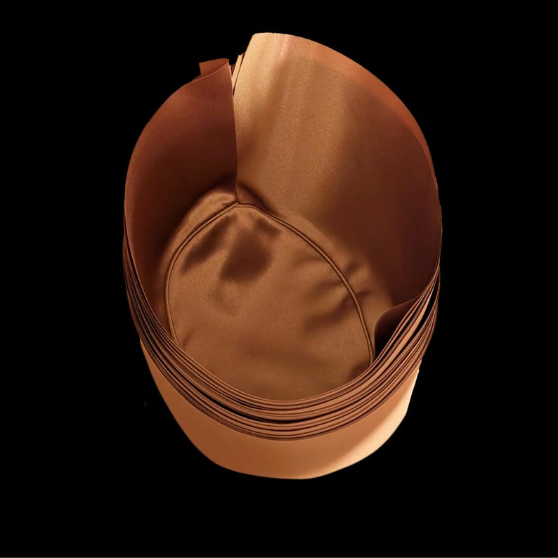 May include: A cylindrical container with a smooth, satin-like copper-colored interior and exterior. The object features a rounded base and vertical walls that curve slightly inward at the top, creating a deep, open-topped vessel with a metallic sheen.