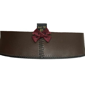May include: A brown leather belt with a burgundy bow and a stitched edge. The belt has a size tag that reads "6S US-S/M".