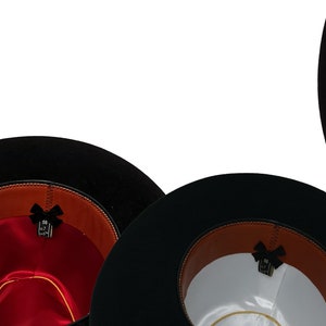 May include: A collection of black wide-brimmed hats shown from the interior. Each hat features a brown leather sweatband, a small black bow detail, and a satin lining in various colors including yellow, red, white, blue, black, and silver.