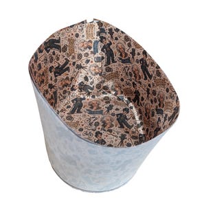 May include: A cylindrical wastebasket with a light gray exterior and an interior lining featuring a repeating pattern of vintage film-themed illustrations, including figures in suits, film reels, cameras, bicycles, and text banners on a tan background.