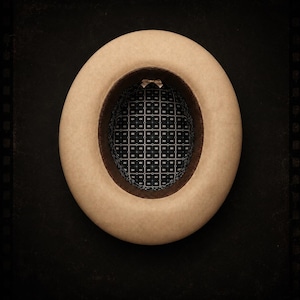 Op de afbeelding: Een bovenaanzicht van een beige vilten hoed met een brede rand. De binnenkant is voorzien van een donkerbruine leren zweetband en een zwarte voering met een herhalend wit geometrisch vierkantpatroon. Bovenaan zit een klein beige strikje.
