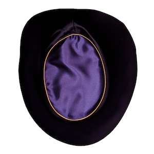 Puede incluir: Un sombrero de fieltro negro con un forro de satén morado y un ribete dorado alrededor del forro.
