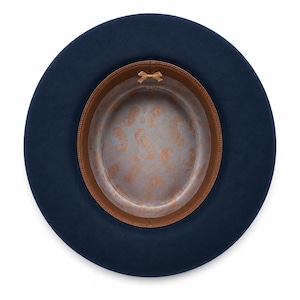 May include: A navy blue fedora hat viewed from above, featuring a wide brim and a smooth exterior. The interior is lined with a light blue fabric displaying a copper-colored paisley pattern, finished with a brown leather sweatband and a small bow.
