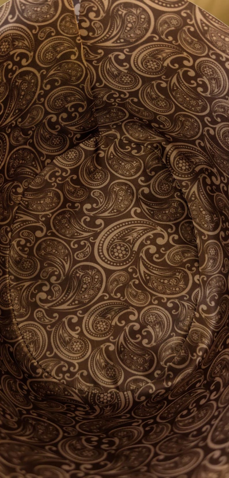 May include: Close-up of a brown fabric with a paisley pattern. The fabric has a soft, textured feel and is perfect for crafting projects.
