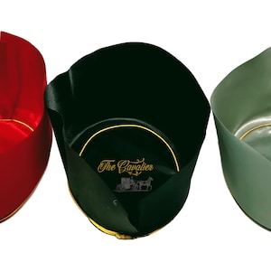May include: Three open-top cylindrical containers in red, black, and sage green. The black container features the gold text The Cavalier with a carriage graphic on the interior base. Each container has a gold-colored circular trim at the base.