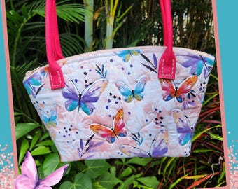 May include: A small pink quilted handbag with a zipper closure and pink handles. The bag is decorated with a butterfly print.