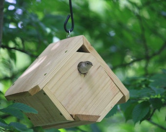 May include: A small wooden birdhouse with a bird inside, hanging from a tree branch. The birdhouse is painted a natural wood color and has a small opening for the bird to enter.