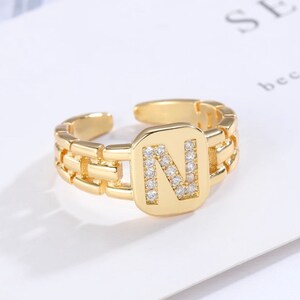 May include: Gold adjustable ring with a square-shaped letter N set with clear cubic zirconia stones.