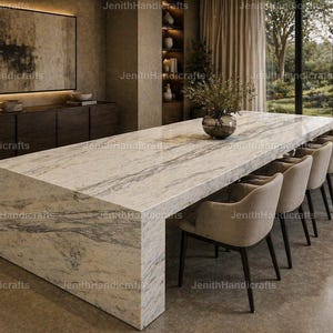 Op de afbeelding: Een grote, rechthoekige marmeren eettafel met een lichtgrijs en wit geaderd patroon. Zes beige gestoffeerde stoelen met zwarte poten zijn aan één kant opgesteld. De tafel staat in een moderne eetkamer.