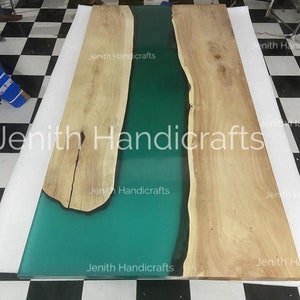 Op de afbeelding: Een groot houten tafelblad met een groene epoxyharsrivier die door het midden loopt. Het tafelblad is gemaakt van natuurlijk hout met een lichtbruine kleur. De epoxyhars is heldergroen en heeft een gladde, glanzende afwerking.