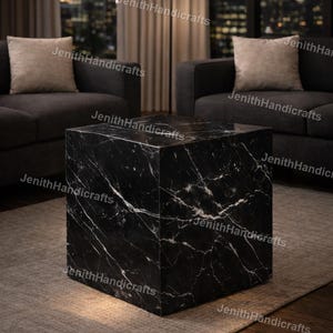 May include: A black marble cube table with white veining, set on a neutral-toned rug. The table is in a living room setting with a lamp and dark gray sofas. The text "JenithHandicrafts" is visible.