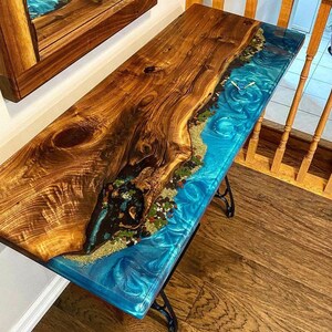 May include: A wooden table with a blue epoxy resin inlay. The resin has a swirling pattern and includes gold and brown accents. The table is supported by a black metal base.