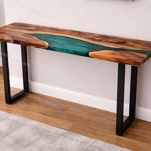 May include: A wooden console table with a live edge design. The tabletop features a river of teal epoxy resin flowing through the center, framed by natural wood. The table is supported by black metal legs.