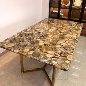 Puede incluir: Mesa rectangular con tapa de piedra pulida con un mosaico de rodajas de ágata marrón, gris y dorada. La mesa tiene una base de metal dorado. Las dimensiones de la mesa son de aproximadamente 183 cm de largo y 91 cm de ancho.