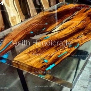 Op de afbeelding: Een houten tafelblad met een heldere epoxyharsafwerking. Het hout heeft een natuurlijke bruine kleur met turquoise blauwe accenten. Het tafelblad wordt ondersteund door een zwart metalen onderstel. "STYLE-4" staat in de linkerbovenhoek van de afbeelding.